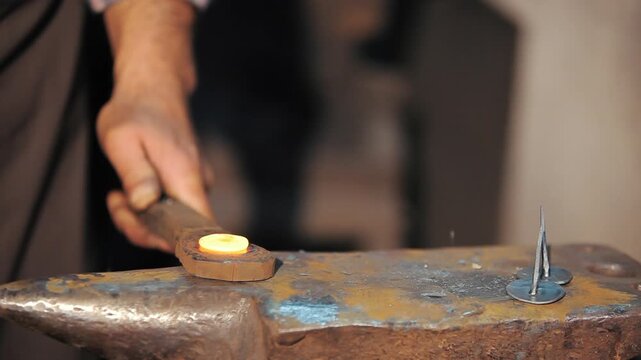 Close-up of a blacksmith hammering a glowing hot piece of iron on an anvil. Traditional metalworking and handmade nail forging concept.