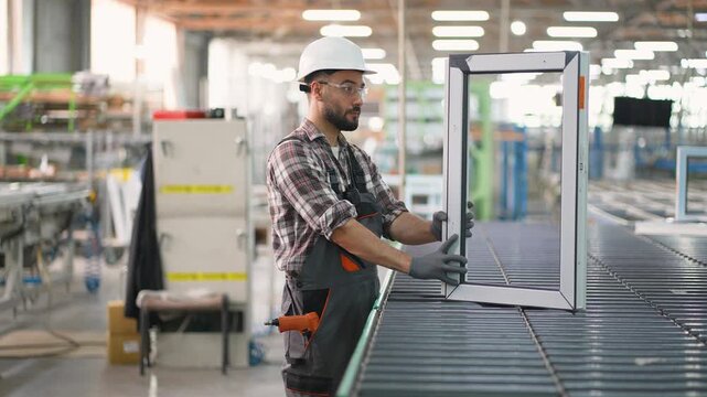 Factory worker assembling plastic window frame on conveyor belt