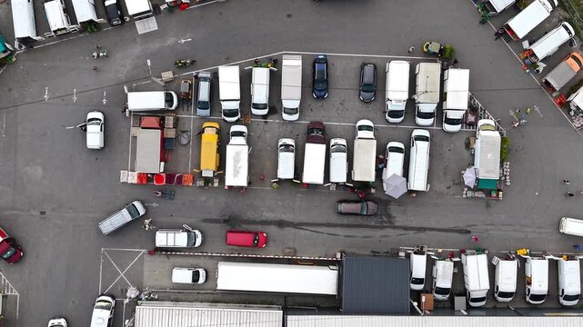 Aerial view of busy farmers market with trucks and vans parked along street. Vibrant produce and bustling activity among vendors and customers. Lively atmosphere of shoppers engaging for fresh produce