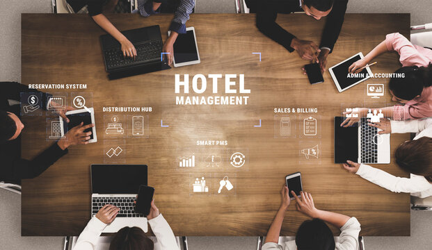 Diverse Group Engaged in Hotel Management Discussion with Digital Devices on Table Displaying Various Software and Icons for Efficient Operations Quark.