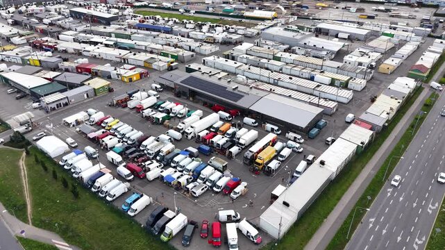 Aerial view of a bustling farmers market with numerous colorful vendor stalls, trucks, and vehicles parked, showcasing a vibrant scene of fresh produce and local goods