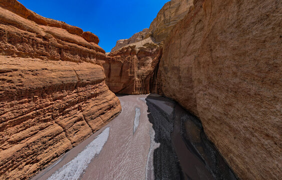 Aerial view of a narrow canyon with steep, layered rock walls and a river flowing through the bottom under a clear blue sky in Nepal.