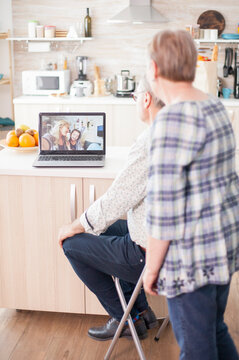 Senior couple uses a laptop for a family video conference in the kitchen, enjoying online conversation and modern communication technology as part of a natural digital communication moment involving.