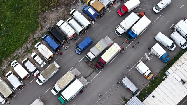 Aerial view of busy farmers market with trucks and vans parked along street. Vibrant produce and bustling activity among vendors and customers. Lively atmosphere of shoppers engaging for fresh produce