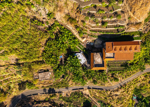 Aerial view of Trilha do Vale do Paul, showing terraced fields, banana plantations, a house with a tiled roof, and a winding road, Faja de Cima, Paul, Cabo Verde.