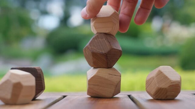 Hand stacking faceted wooden stones playing Tumi Ishi game of balance and mindfulness