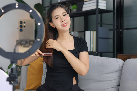 Young Asian woman showing hair tutorial in front of phone camera and ring light.