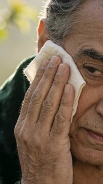 Vertical video: Bringing white cloth, senior dabbing right cheek in garden, drying face, green robe