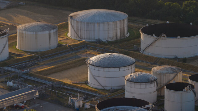 Aerial view of the Tanklager fuel storage facility with large white cylindrical tanks surrounded by earthen berms and industrial infrastructure in Hunxe, North Rhine-Westphalia, Germany.