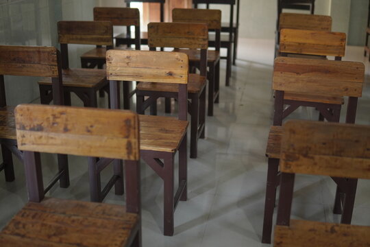 Rows of empty vintage wooden school chairs lined up in a quiet, traditional classroom setting.