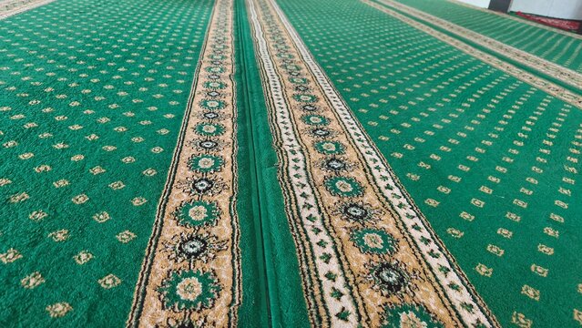 Green prayer carpet with intricate traditional Islamic patterns laid out inside a mosque interior.