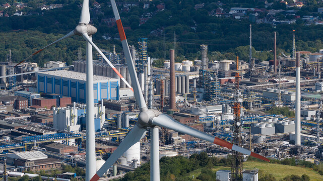 Aerial view of a wind turbine in the foreground with an industrial tank farm and refinery complex in the background in Gelsenkirchen, North Rhine-Westphalia, Germany.