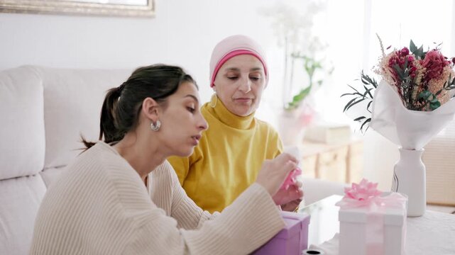 Daughter supporting mother with cancer wrapping presents together at home