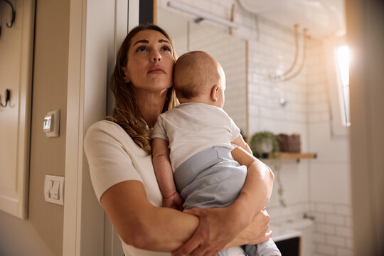 Young mother going through postpartum depression while holding her baby at home.