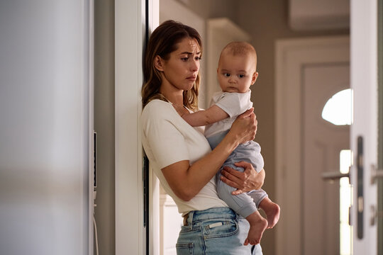 Young mother experiencing postpartum depression while holding her baby son at home.