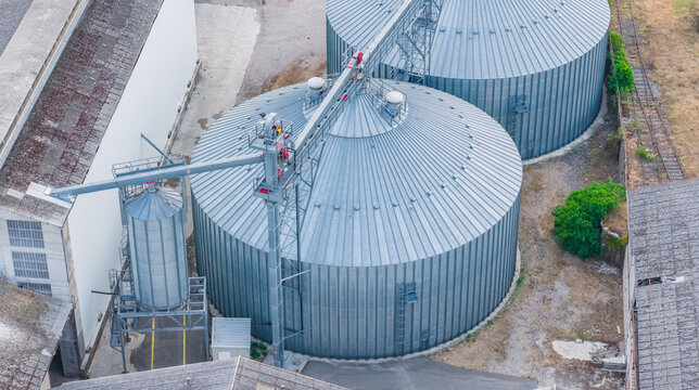 Aerial view of large galvanized grain silos with conveyor systems at an agricultural storage facility in Le Pouzin, Auvergne-Rhone-Alpes, France.