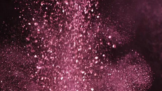 Pink shimmering powder falling against dark textured background