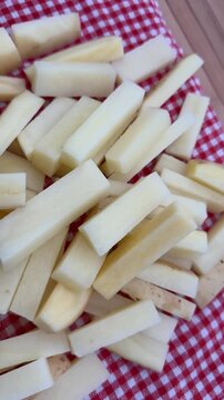 Raw French Fries French-Cut Potatoes on Red Plaid Background 4K. High-angle shot of freshly cut, raw potato sticks prepared for French fries, piled on a traditional red and white checkered tablecloth.