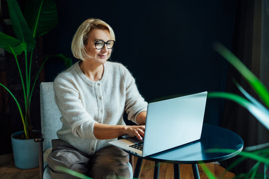 Portrait of 50's stylish, confident mature businesswoman, middle aged experienced senior female professional, business coach, mentor, therapist, counselor working on laptop in office. Female leader