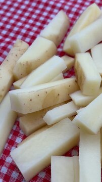 Raw French Fries French-Cut Potatoes on Red Plaid Background 4K. High-angle shot of freshly cut, raw potato sticks prepared for French fries, piled on a traditional red and white checkered tablecloth.