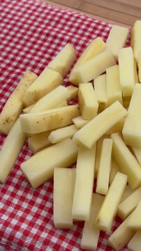 Raw French Fries French-Cut Potatoes on Red Plaid Background 4K. High-angle shot of freshly cut, raw potato sticks prepared for French fries, piled on a traditional red and white checkered tablecloth.