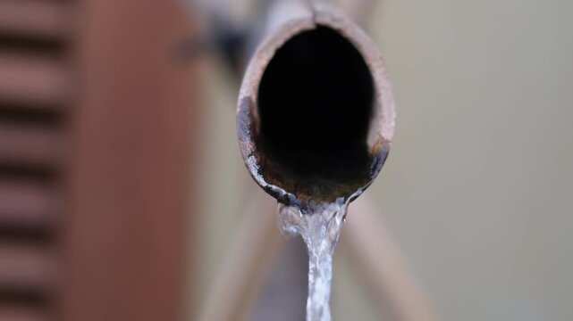 Extreme close up of water dripping from a pipe conceptualizing drought and water scarcity
