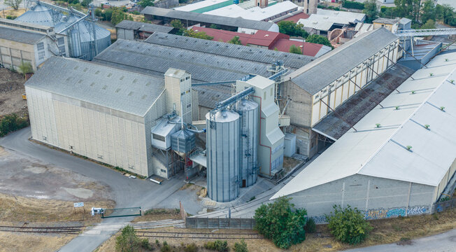 Aerial view of an industrial grain storage and processing facility with metal silos, warehouses, and conveyor systems in Le Pouzin, Auvergne-Rhone-Alpes, France.
