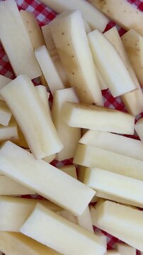 Raw French Fries French-Cut Potatoes on Red Plaid Background 4K. High-angle shot of freshly cut, raw potato sticks prepared for French fries, piled on a traditional red and white checkered tablecloth.
