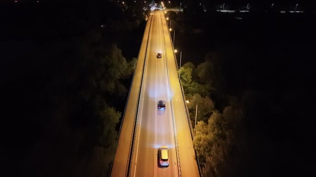 Aerial view of a cars driving on a well-lit road at night, showcasing illuminated path and surrounding dark landscape, capturing the essence of a nighttime city drive. Auto riding at evening route way