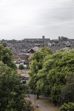 Aerial view of the historic city of York, featuring dense residential rooftops, lush green trees, and a pathway with people walking, in York, England, United Kingdom.