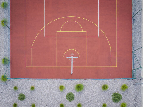 Aerial view of a basketball court with a red surface and yellow markings, surrounded by a gravel border and green bushes in Wieliczka, Lesser Poland Voivode, Poland.