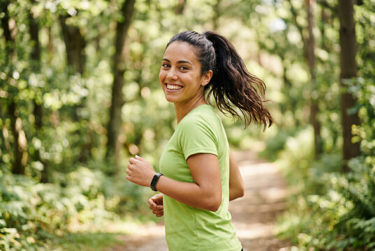 Cheerful young woman jogging along a forest trail looking back with a bright smile