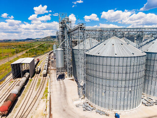 View of grain silos and trains at a large agricultural site during a sunny day with blue sky and clouds © DSMT