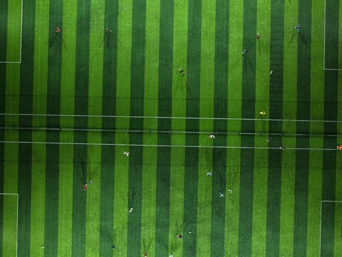 Aerial view of Bravo Arena soccer field with players in motion on the green pitch in Kecamatan Denpasar Selatan, Bali, Indonesia.