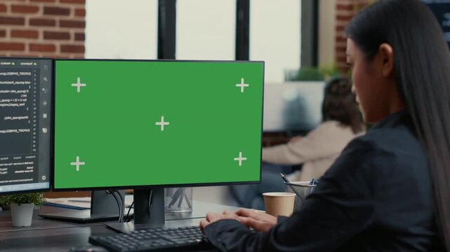Asian programmer develops software at a computer with an editable green screen display, linking coding workflow, mockup design and compositing