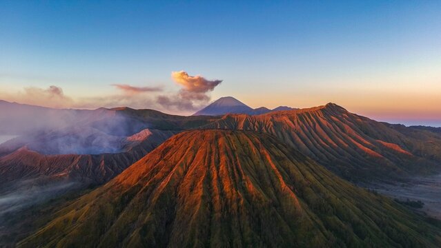 Aerial view of Mount Bromo with its smoking crater and rugged volcanic ridges illuminated by the warm light of golden hour in Tosari, East Java, Indonesia.