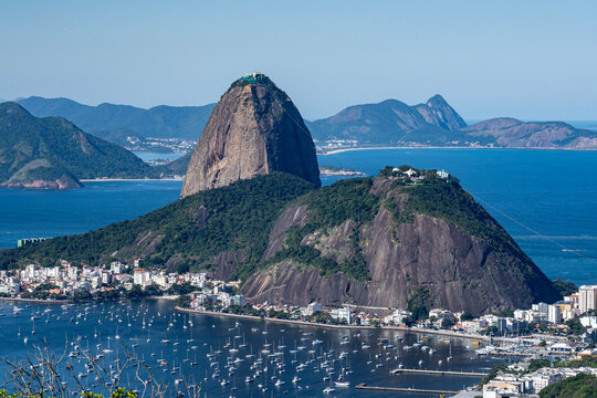 The sweeping view of Sugarloaf Mountain highlights its imposing shape rising above Guanabara Bay, featuring green slopes, blue waters, and the sprawling city. Rio de Janeiro, Brazil.