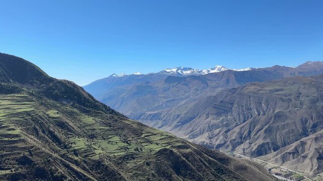 Broad mountain valley view with layered terraced hills, rough gray rock textures, patchwork fields, dark forest cover, and sunlit foreground ledge, creating calm outdoor travel mood and strong sense