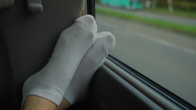 Woman relaxing with her feet on bus or car window during a long road trip. Highway passing by in background. Hippie or traveler tired and sleeping during ride or hitchhiking to destination