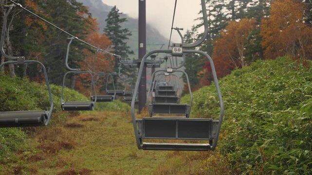 Empty chairlift moving over a vibrant autumnal forest on a foggy day at Daisetsuzan Sounkyo Kurodake Ropeway in Hokkaido, Japan. Beautiful scenery for tourism and travel in a famous national park