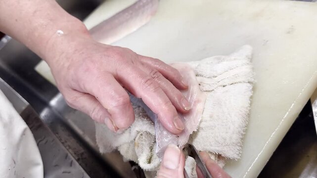 Chef removing pin bones from fresh Japanese sea bass fillet, Japan