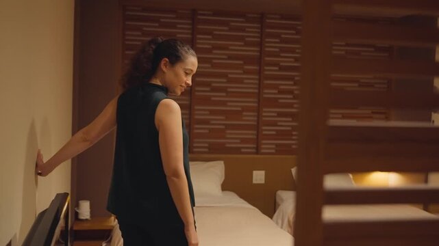Young woman with curly hair walking into her hotel room, smiling as she looks at the cozy and modern interior design with twin beds, expressing satisfaction and happiness for her accommodation