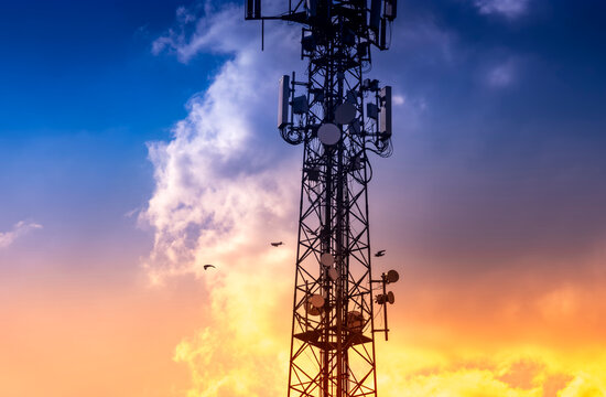 Telecommunication tower silhouette against sunset sky. Birds fly past the cellular antennas. Highlighting the connection between technology and nature.