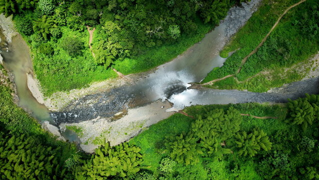 Aerial view of a winding river flowing through a lush green forest with dense vegetation, rocky riverbanks, and clear water in San Sebastian, San Sebastian, Puerto Rico.