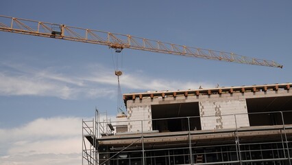 Ujęcie pod kątem przedstawiające fragment powstającego budynku w stanie surowym z rusztowaniem oraz ukośne ramię żurawia budowlanego na tle nieba. © tomo81