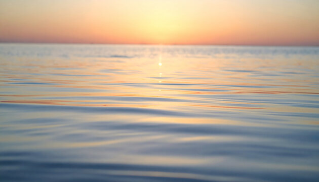 Ocean water surface ripples reflecting a warm golden sunset glow at twilight with soft focus blurred background horizon view