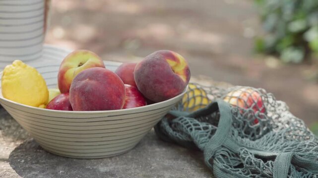 Close-up of Hand Selecting Fresh Peaches from Bowl