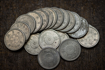 A stacked collection of vintage Japanese 10 sen coins from the Showa era, arranged on a dark wooden surface with worn aluminum texture, aged patina, chrysanthemum motifs, and Japanese script. © Mr