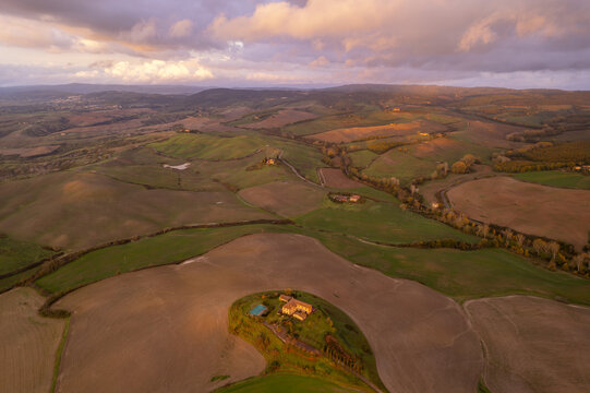 Aerial view of the rolling hills of the Crete Senesi landscape with a farmhouse on a hill during golden hour in Asciano, Tuscany, Italy.