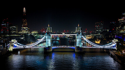 Night aerial view of Tower Bridge illuminated over the River Thames with London's skyline and city lights creating a striking urban scene. © Francois Quartiers